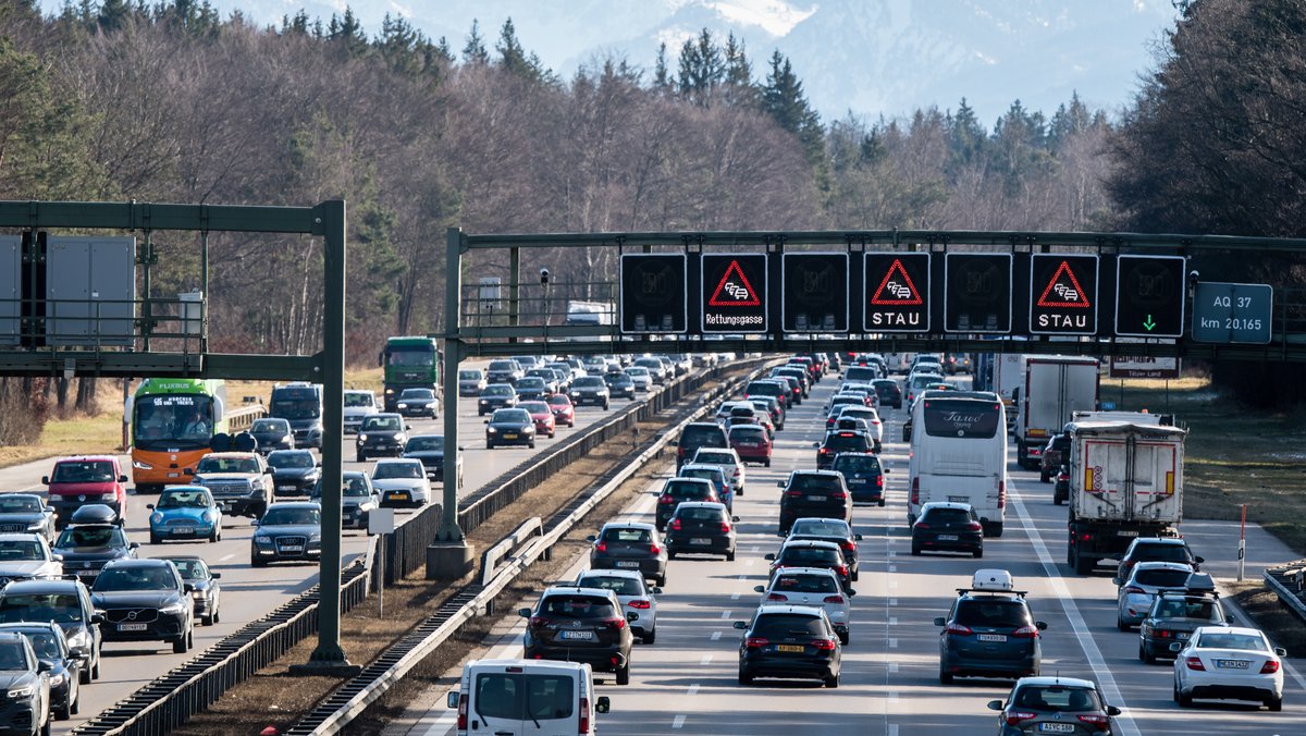 Dichter Verkehr schiebt sich über die Autobahn 8 in Fahrtrichtung Salzburg und Brenner-Autobahn im Hofoldinger Forst, während über der Straße auf einer digitalen Anzeige vor Stau gewarnt wird.