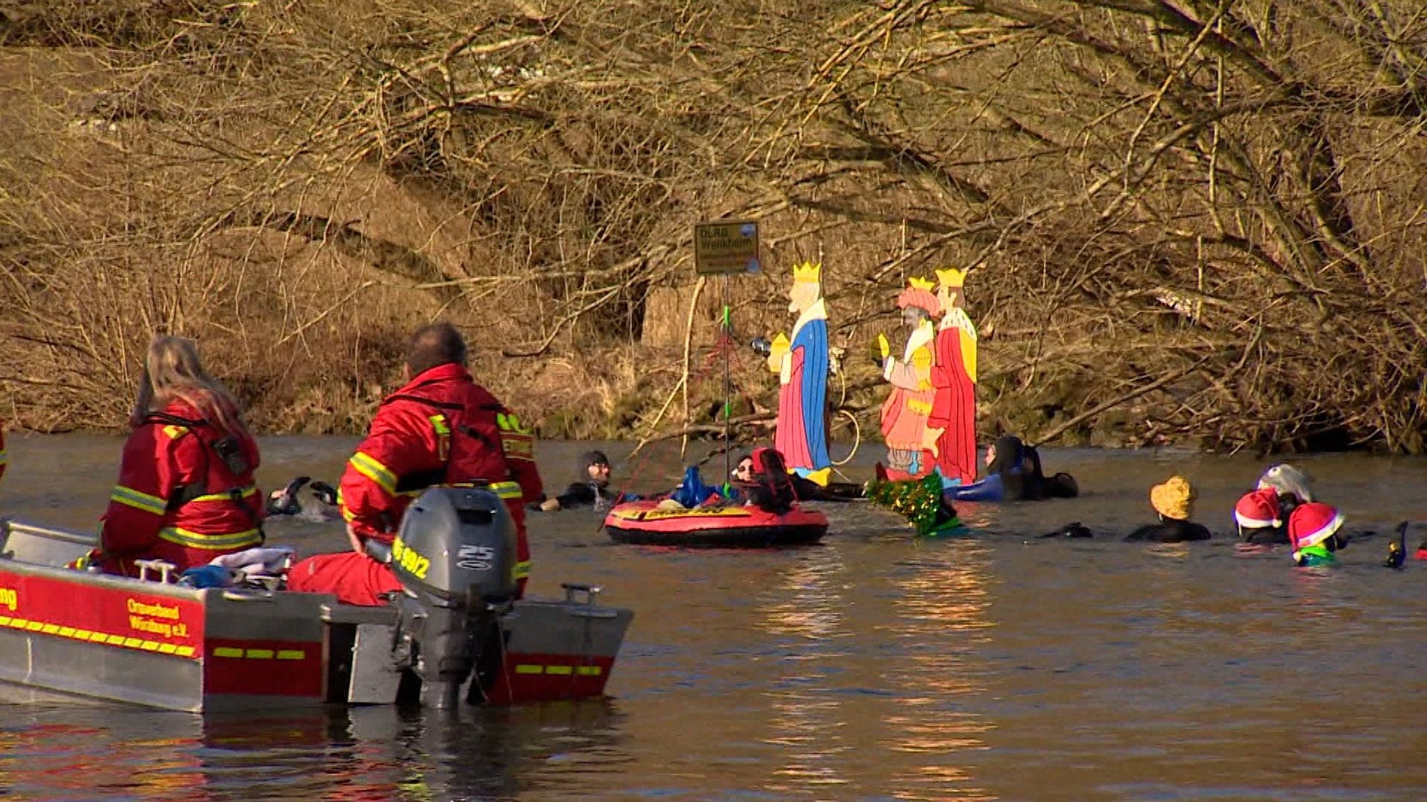 Mehrere Schwimmerinnen und Schwimmer im Neopren-Anzug im Main bei Würzburg, daneben ein DLRG-Boot.