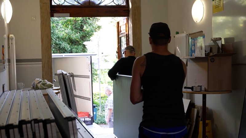 Zwei Männer tragen eine Tafel. | Bild: BR Zwei Männer tragen eine Tafel.