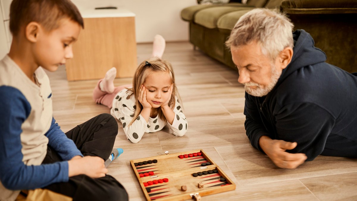 Ein Mann spielt mit zwei Kindern ein Brettspiel. 