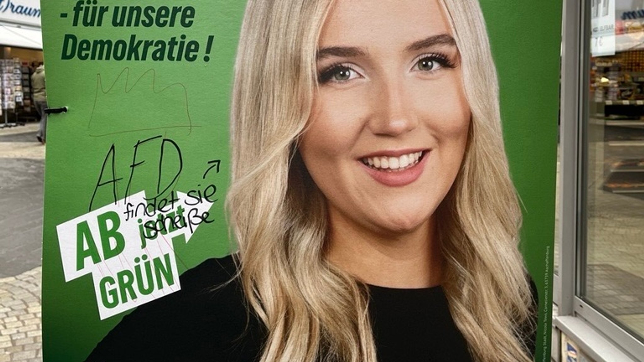 Das BR-Bild aus Aschaffenburg zeigt die Schmiererei sowie den Schriftzug auf dem Wahlplakat.