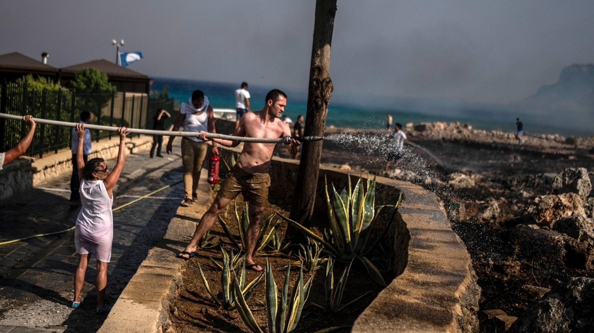 Ein Mann versucht zusammen mit anderen Menschen, ein Feuer in der Nähe des Badeortes Lindos auf der Ägäisinsel Rhodos zu löschen. 