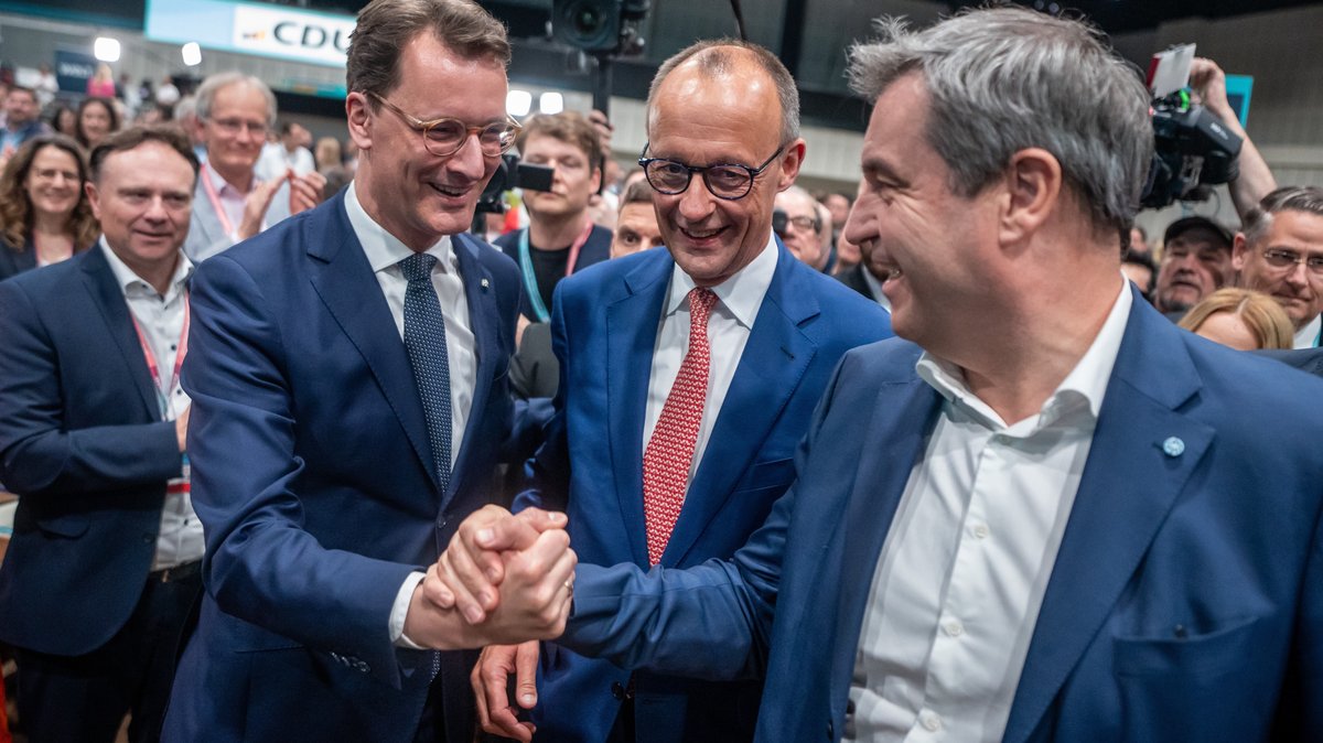 Berlin, 07.05.24: CDU-Chef Merz (Mitte), NRW-Ministerpräsident Wüst (l.) und CSU-Chef Söder (r.) - alle in blauen Sakkos über weißem Hemd, Wüst und Merz auch mit Krawatte, beim CDU-Bundesparteitag. Wüst und Söder packen sich an der jeweils rechten Hand.