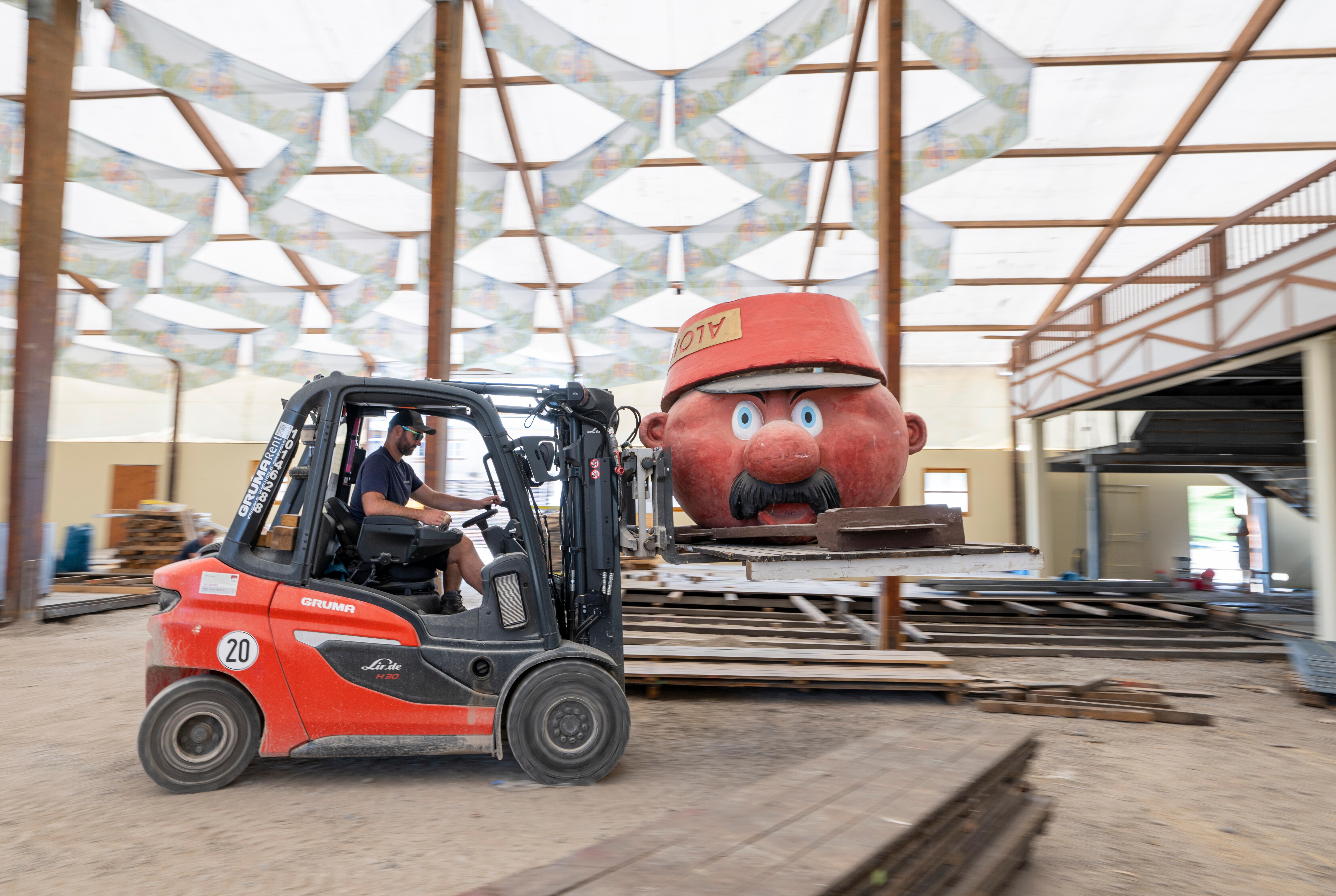 Beim Aufbau der Wiesn wird der Pappmascheekopf des Alois Hingerl mit einem Flurförderzeug durch die Gegend gefahren. | Bild:picture alliance/dpa/Peter Kneffel
