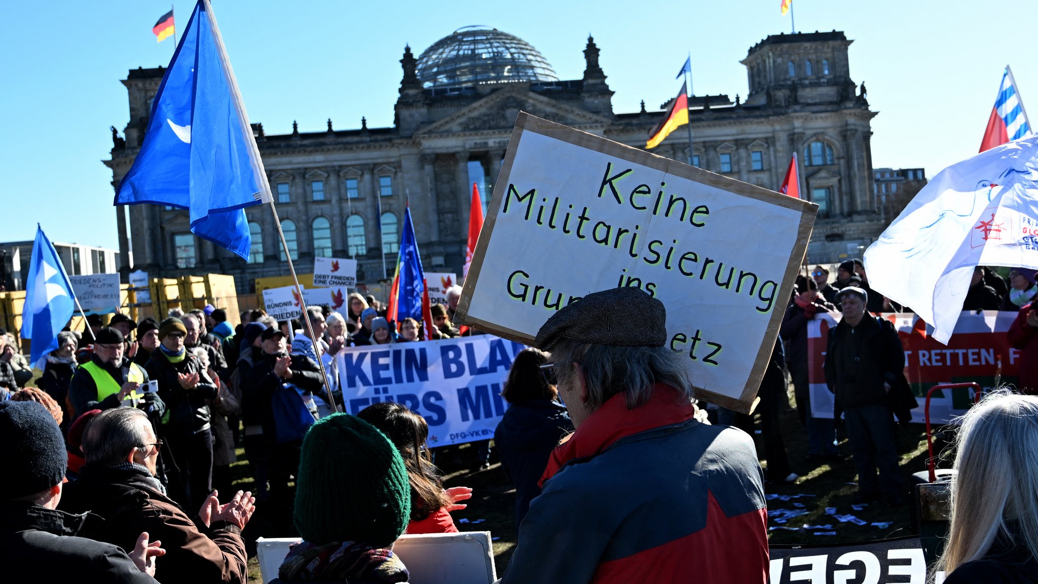 Ein Demonstrant hält ein Plakat hoch, auf dem steht "Keine Militarisierung im Grundgesetz" während eines Protests gegen eine Erhöhung der Verteidigungsausgaben vor dem Bundestag am 18. März 2025 in Berlin 
