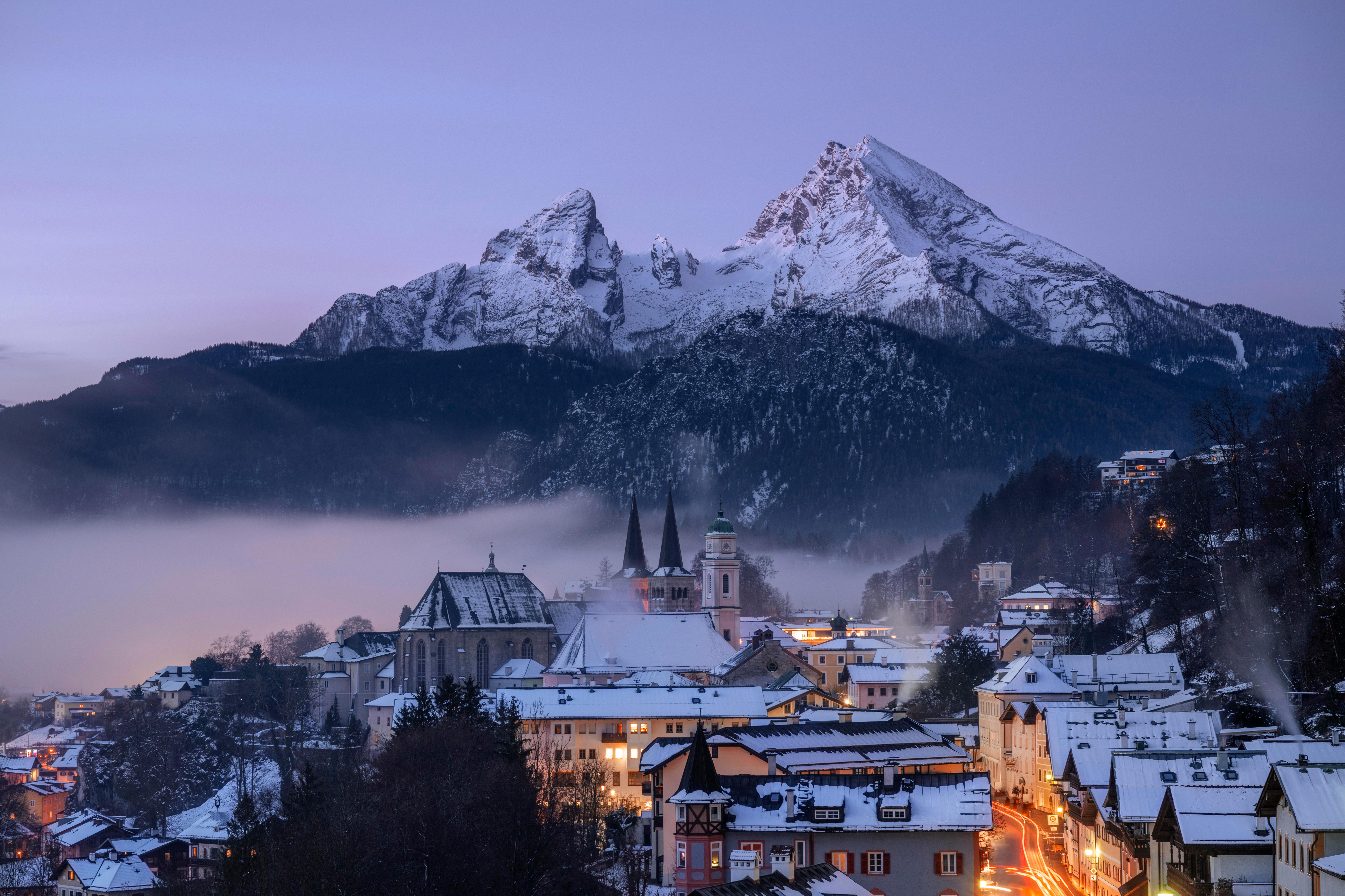 Ansicht vom verschneiten Berchtesgaden im Halbdunkel mit erleuchteten Fenstern und Straßen, dahinter der verschneite Watzmann. (Archivbild)