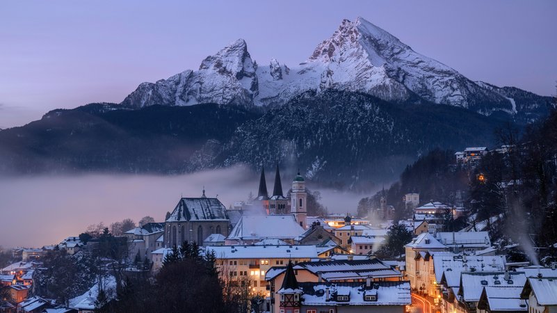 Ansicht vom verschneiten Berchtesgaden im Halbdunkel mit erleuchteten Fenstern und Straßen, dahinter der verschneite Watzmann. (Archivbild) | Bild: picture alliance / Westend61 | Martin Rügner Ansicht vom verschneiten Berchtesgaden im Halbdunkel mit erleuchteten Fenstern und Straßen, dahinter der verschneite Watzmann. (Archivbild)