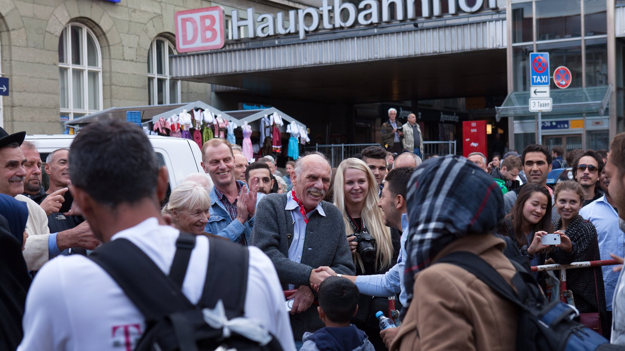 Zwei Männer schütteln Hände und sind am Hauptbahnhof von vielen Menschen umringt | Bild: picture alliance/SZ Photo/Florian Peljak Zwei Männer schütteln Hände und sind am Hauptbahnhof von vielen Menschen umringt