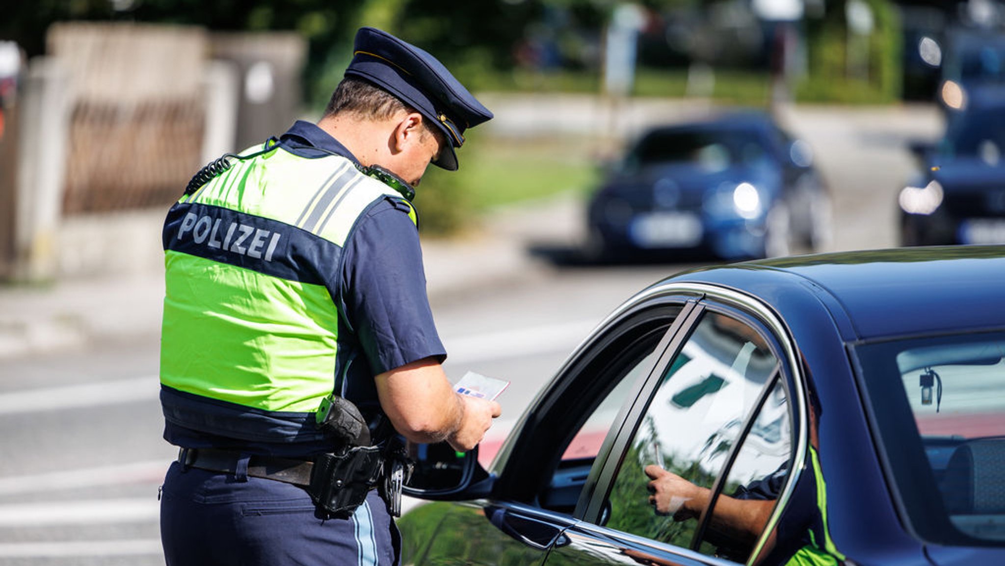 Eine Polizist der Bayerischen Grenzpolizei kontrolliert bei einem Pressetermin an einer Kontrollstelle die Dokumente eines Autofahrers.