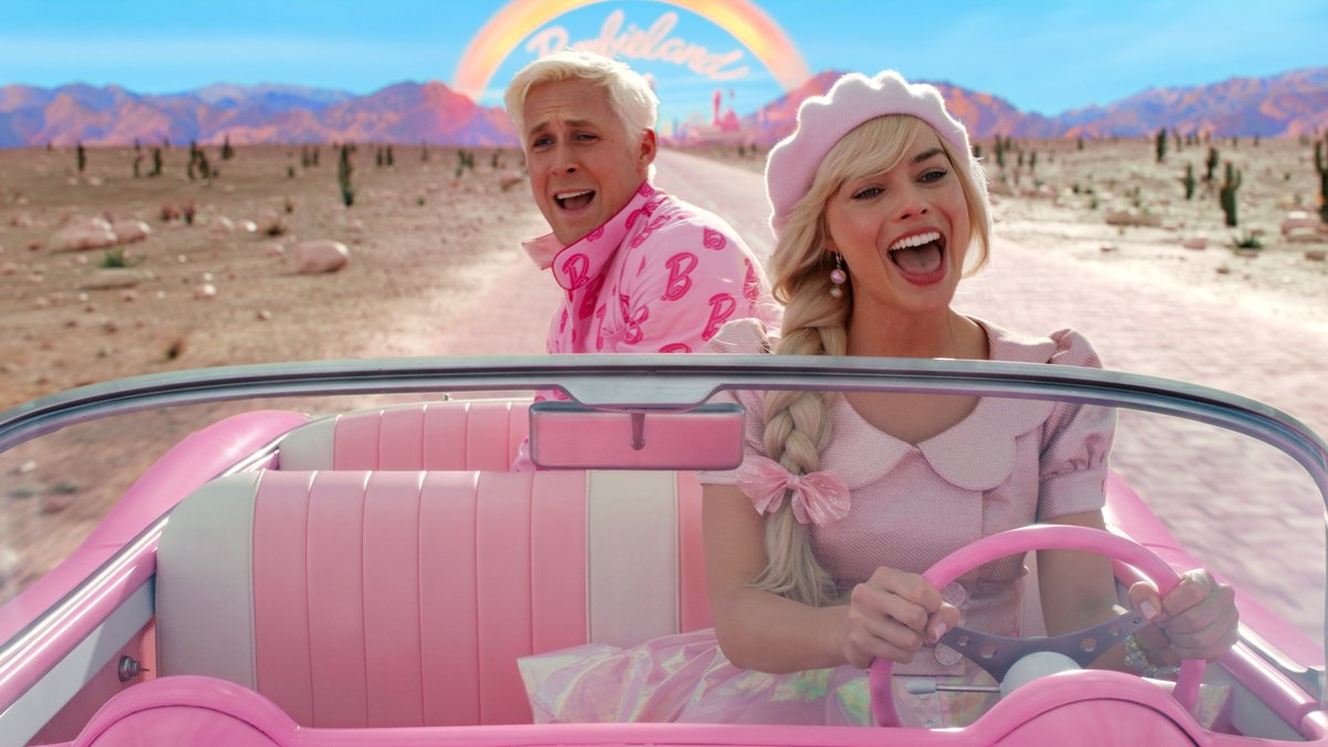 Barbie (Margot Robbie) und Ken (Ryan Gosling) fahren in einem rosafarbenen Cabriolet eine Wüstenstraße entlang und singen dabei gutgelaunt ein Lied
