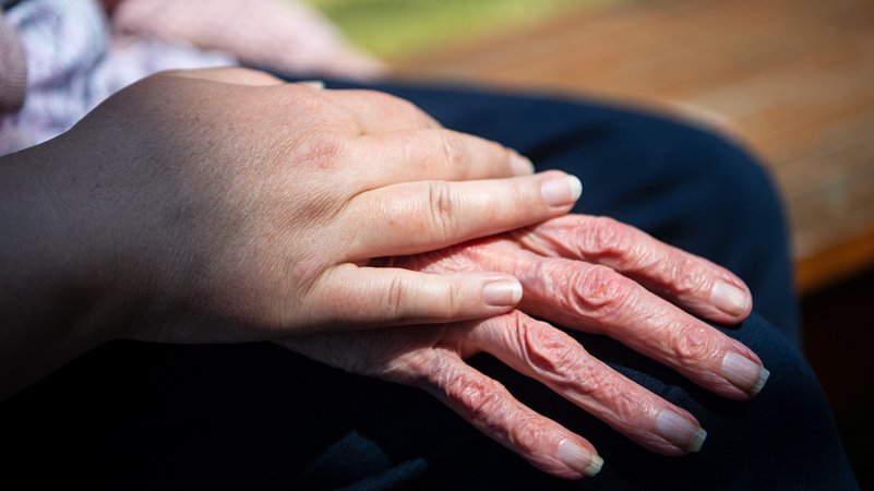Die Hand einer Pflegefachkraft liegt auf der Hand einer Bewohnerin eines Seniorenheims 