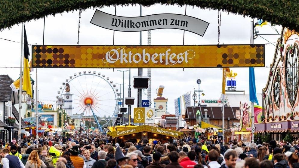 ARCHIV (05.10.2025). Symbolbild eingang Oktoberfest. Zahlreiche Besucher gehen am 05.10.2025 am frühen Morgen kurz nach der ffnung durch das Tor vom Haupteingang auf das 190. Oktoberfest auf der Theresienwiese in München (Bayern, Deutschland), während im Hintergrund die Bierzelte (Festzelte) der Brauereien und das Riesenrad zu sehen sind. 