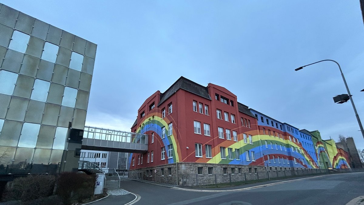 Ein Firmengebäude des Porzellanherstellers Rosenthal mit der markanten Regenbogenfassade, davor eine menschenleere Straße. 