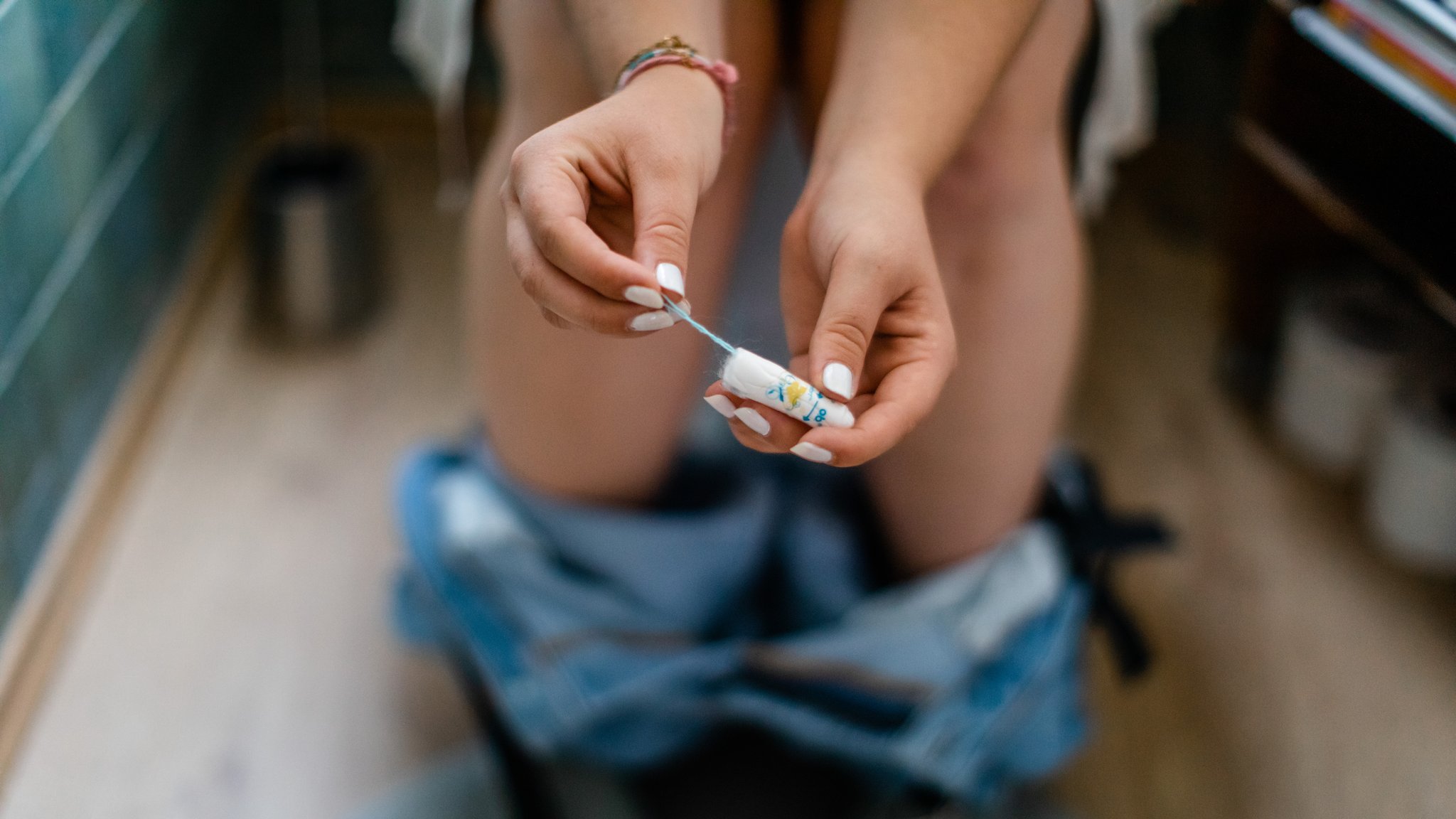 Eine junge Frau mit einem Tampon auf der Toilette.