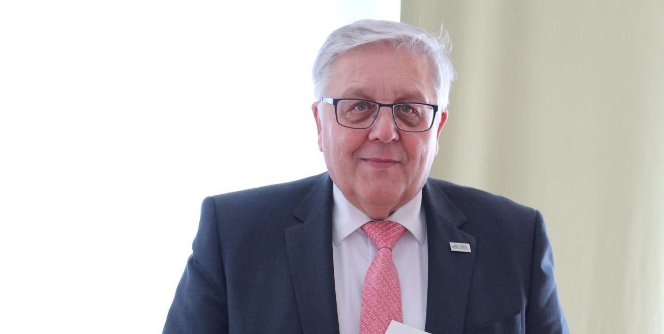 Ein weißhaariger Mann lächelt und schaut in die Kamera.