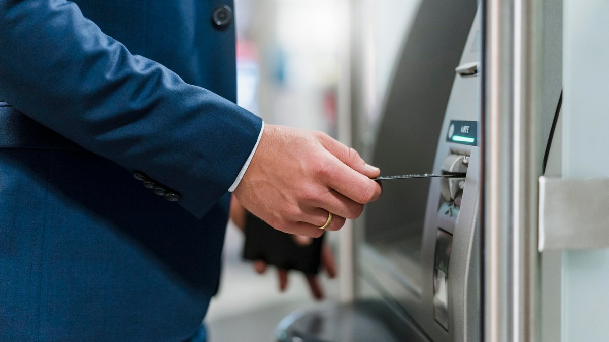Ein Mann im Anzug steckt eine Bankkarte in den Geldautomaten.
