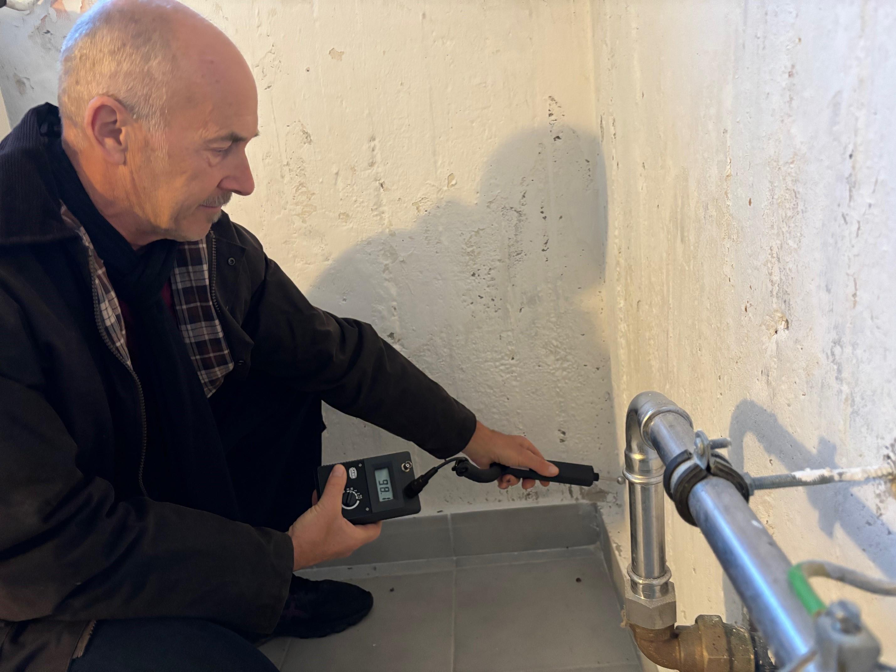 Mann hält Feuchtemessgerät an eine Kellerwand