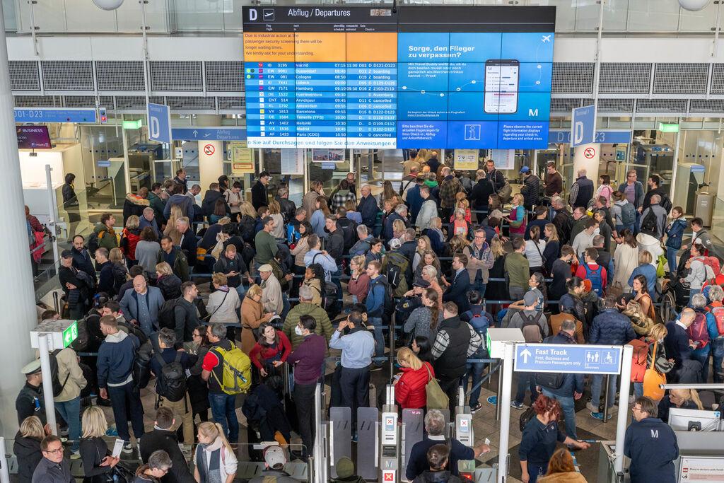 Passagiere am Münchner Flughafen stehen in der Abflughalle in Schlangen an 