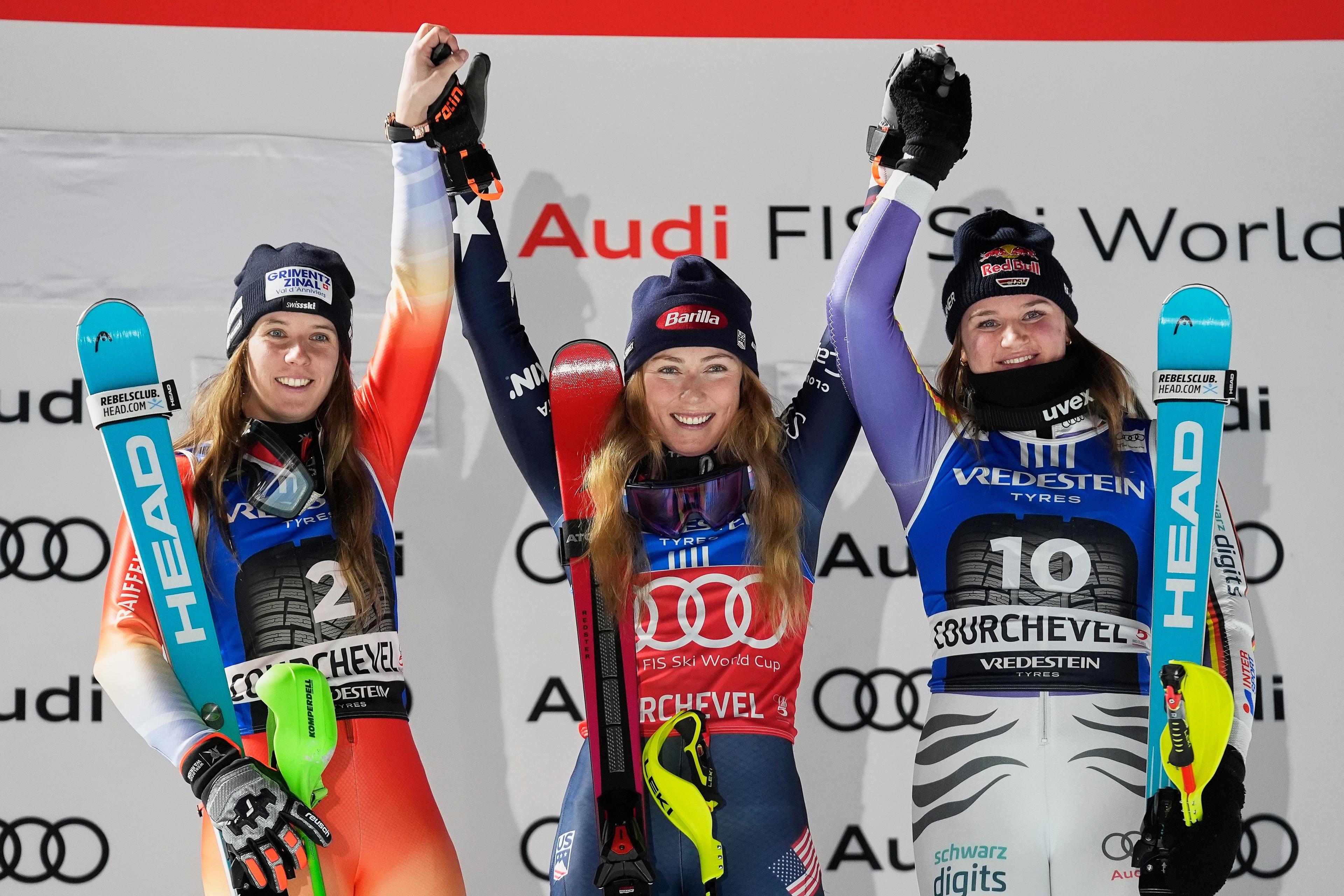 16.12.2025, Frankreich, Courchevel: Mikaela Shiffrin (M, USA) jubelt auf dem Podium neben der zweitplatzierten Camille Rast (l, Schweiz) und der drittplatzierten Emma Aicher (Deutschland) über ihren Sieg beim alpinen Skiweltcup-Slalom der Damen. Foto: Giovanni Auletta/AP/dpa +++ dpa-Bildfunk +++