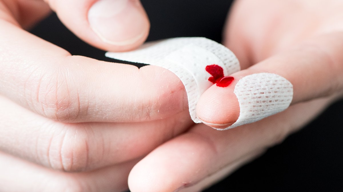 Zwei Hände in Nahaufnahme: Ein Pflaster wird um einen leicht blutenden Finger gewickelt