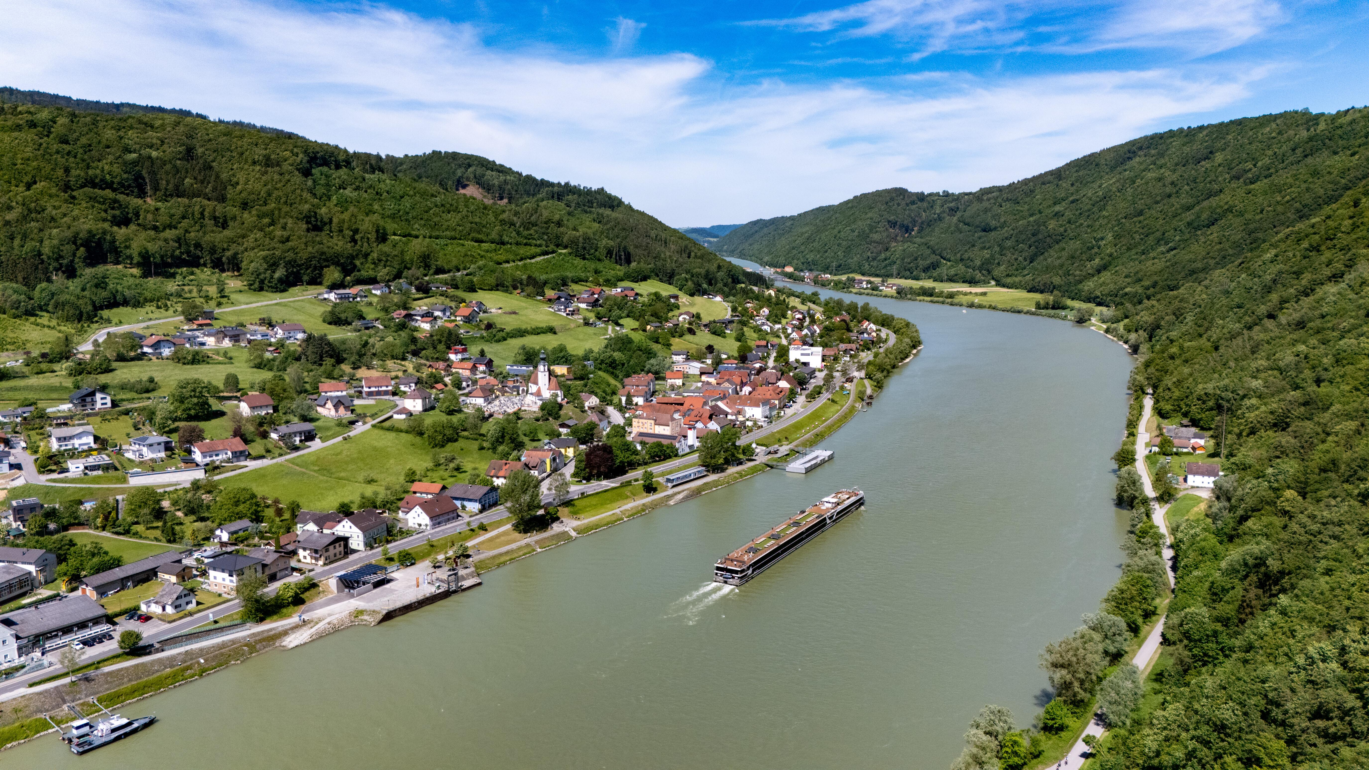 Die Donau bei Engelhartszell in Österreich (Archivbild), auf dem Fluss fährt ein flaches Lastenschiff.