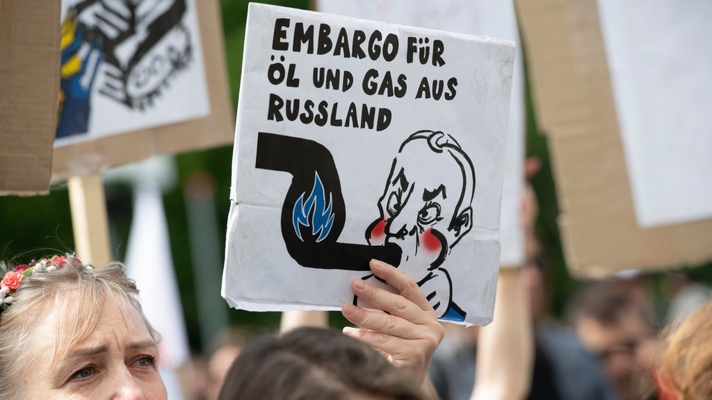 Bei einer Demonstration hält eine Frau ein Plakat hoch. Darauf steht: "Embargo für Öl und Gas aus Russland". 