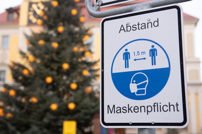 Archivbild: 23.12.2020, Sachsen, Bautzen: Ein Hinweisschild für die Maskenpflicht und den Abstand hängt am Marktplatz vor einem Weihnachtsbaum. 