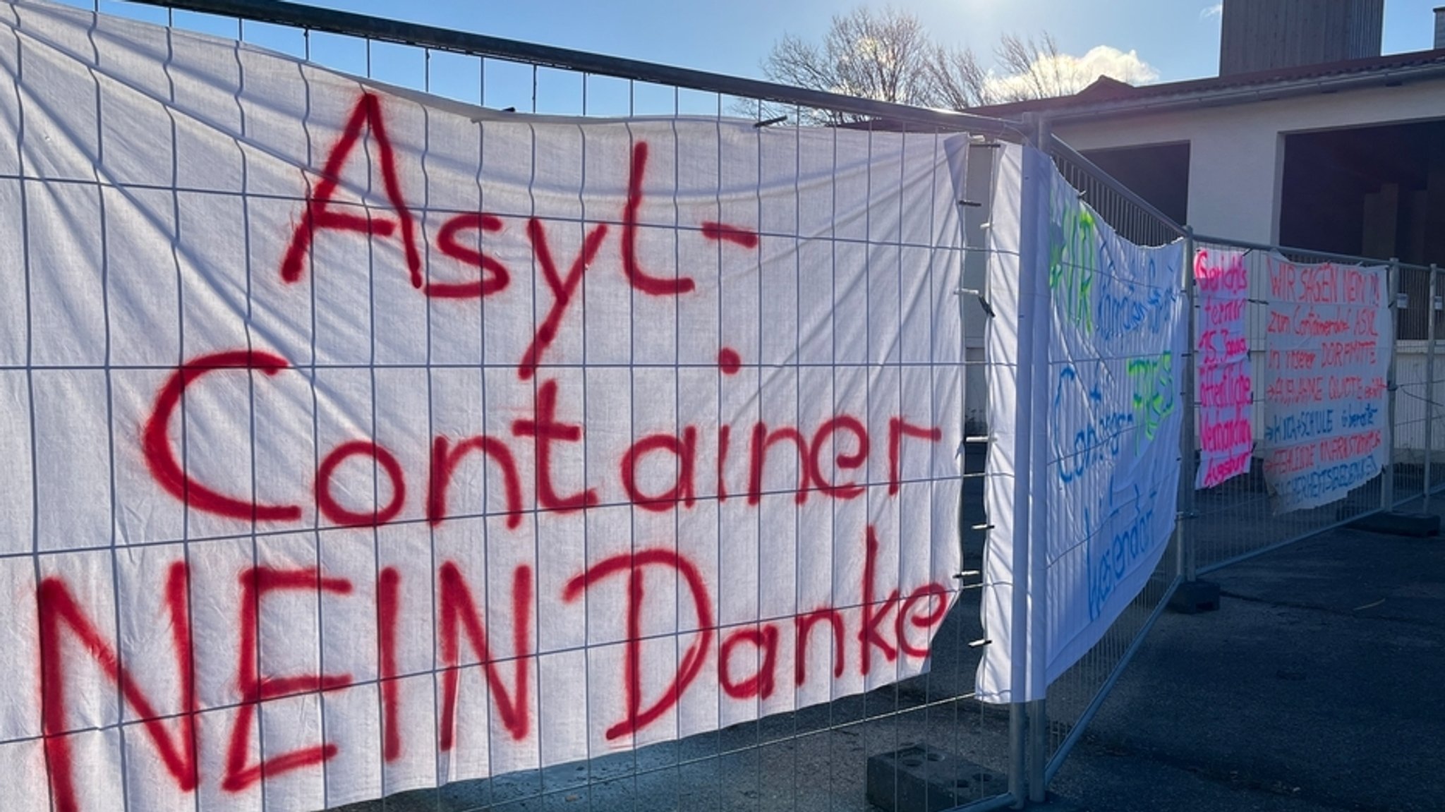 An einem Bauzaun hängen Leintücher mit Protestaufschriften gegen eine Flüchtlingsunterkunft in Westendorf