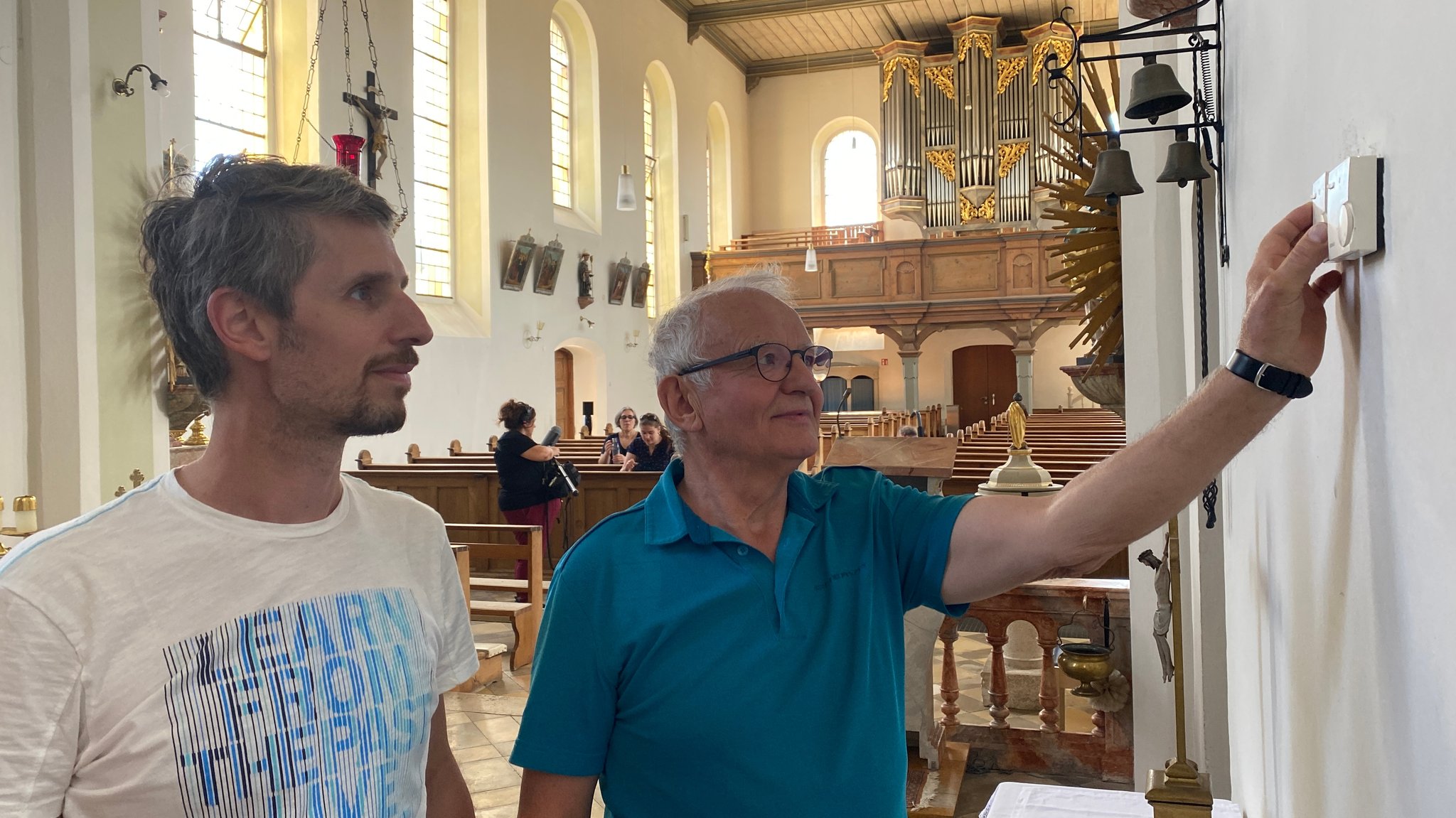 Zwei Männer stehen im Kirchenraum am Temperaturregler.