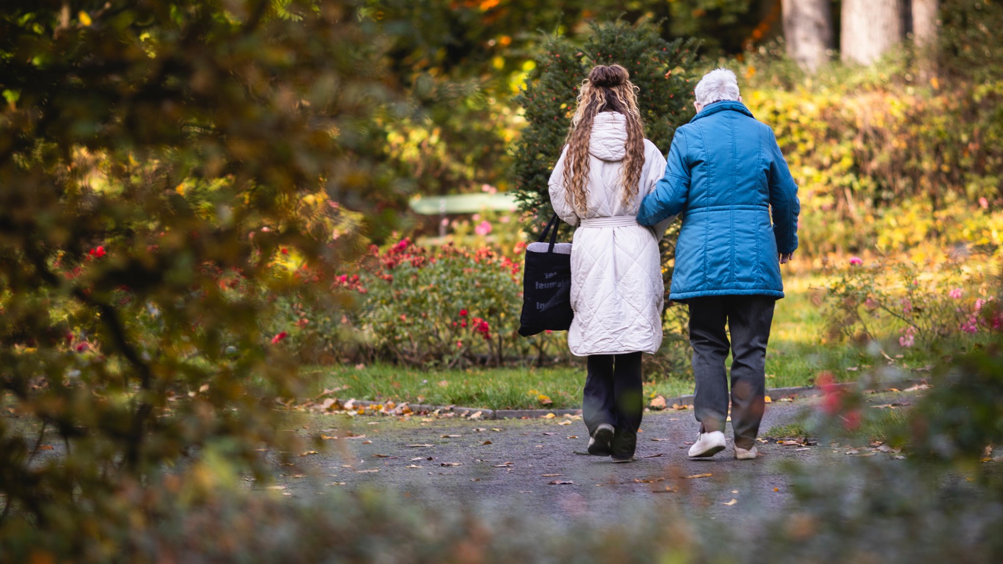Eine junge Frau und eine Seniorin machen einen morgendlichen Spaziergang durch einen Park.