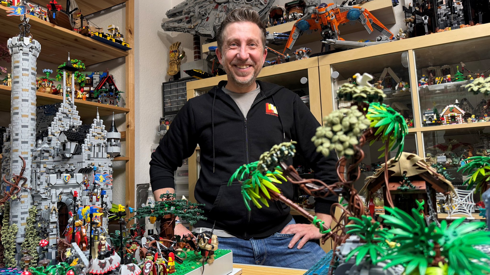 Thomas Gottwald steht lachend hinter Lego-Palmen und einer Lego-Ritterburg. | Bild: BR/ Birgitt Roßhirt Thomas Gottwald steht lachend hinter Lego-Palmen und einer Lego-Ritterburg.