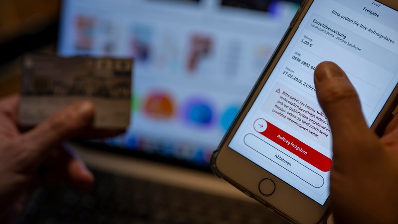 (Symbolbild) Ein Mann überweist in einer Banking-App auf einem Smartphone Geld, während im Hintergrund auf einem Laptop die Seite eines Online-Handels angezeigt wird. | Bild: dpa/pa/Monika Skolimowska (Symbolbild) Ein Mann überweist in einer Banking-App auf einem Smartphone Geld, während im Hintergrund auf einem Laptop die Seite eines Online-Handels angezeigt wird.