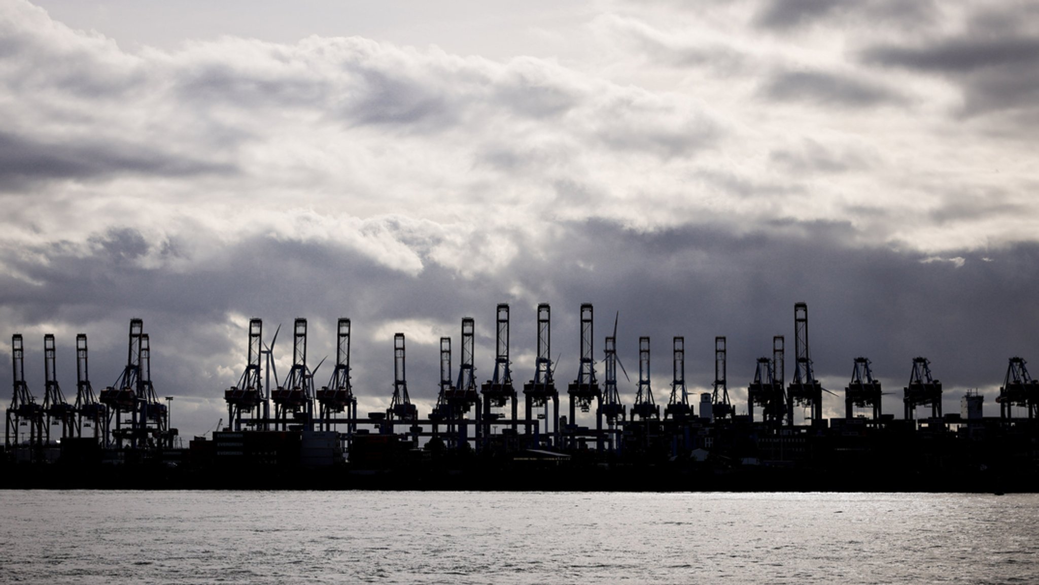 Containerbrücken der Terminals Burchardkai und Eurogate in Hamburg sind als Silhouetten im Hafen an der Elbe zu sehen