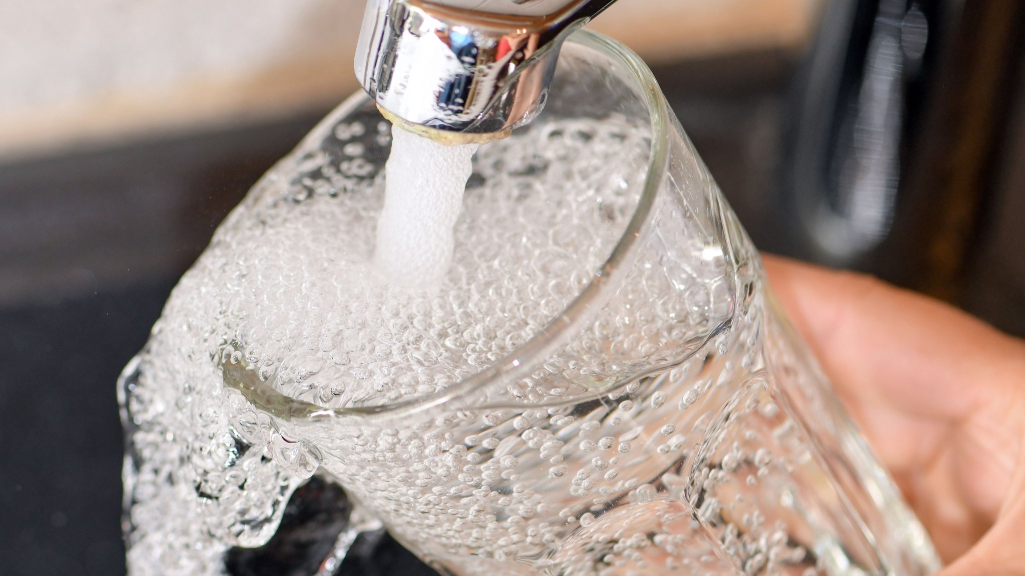 Eine Frau hält ein Glas Wasser unter den Wasserhahn.