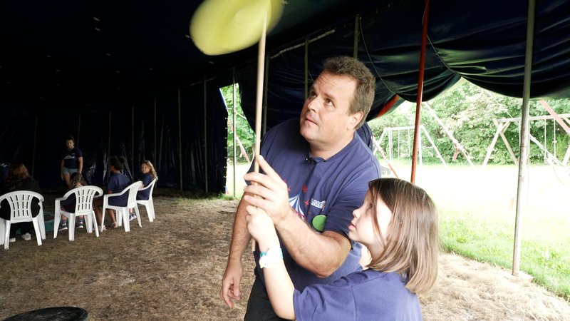 Ein Mann übt gemeinsam mit einem Kind, einen Teller auf einem Stab zu drehen | Bild: Lea Weinberg/BR Ein Mann übt gemeinsam mit einem Kind, einen Teller auf einem Stab zu drehen