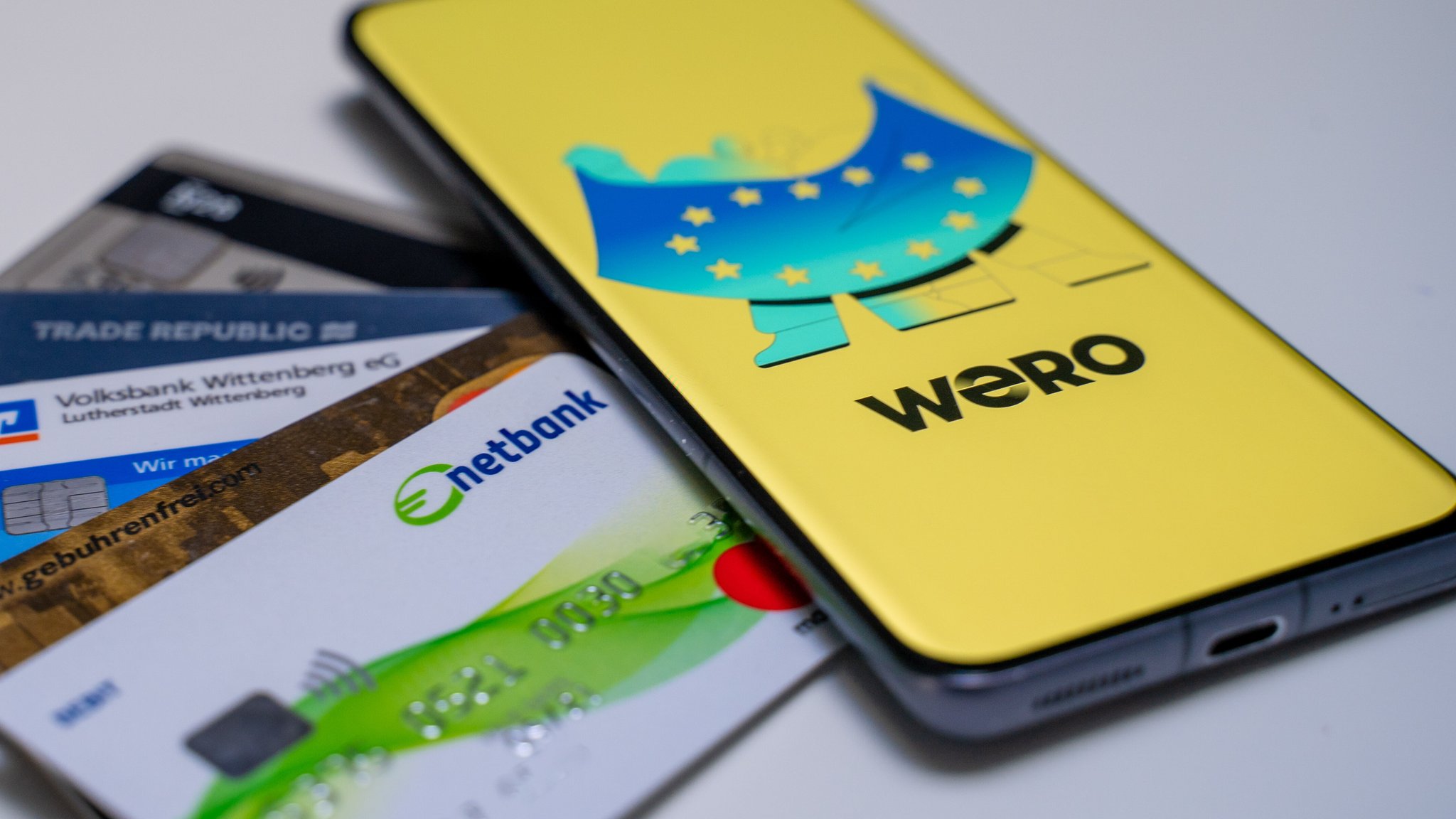 Smartphone mit geöffneter Wero-App und einigen Bankkarten im Hintergrund