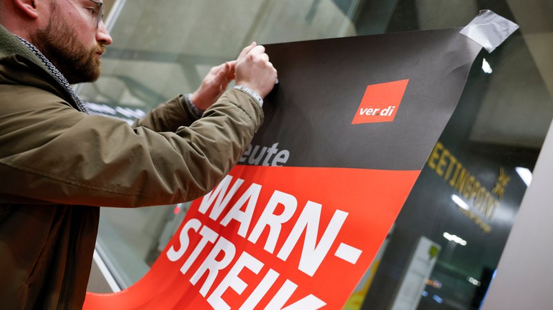 Ein Mann klebt ein Plakat mit der Aufschrift «Heute Warn-Streik» an eine Scheibe | Bild: dpa-Bildfunk/Thomas Banneyer Ein Mann klebt ein Plakat mit der Aufschrift «Heute Warn-Streik» an eine Scheibe