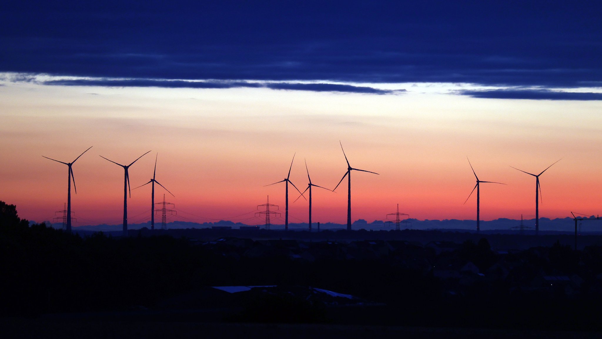 Windräder stehen unter einer Wolkenwand im Sonnenaufgang