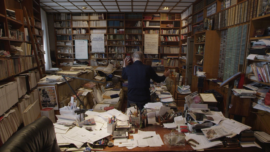 Ennio Morricone von hinten, wie er in seinem über und über mit Papieren und Büchern angefülltem Arbeitszimmer "luftdirigert".