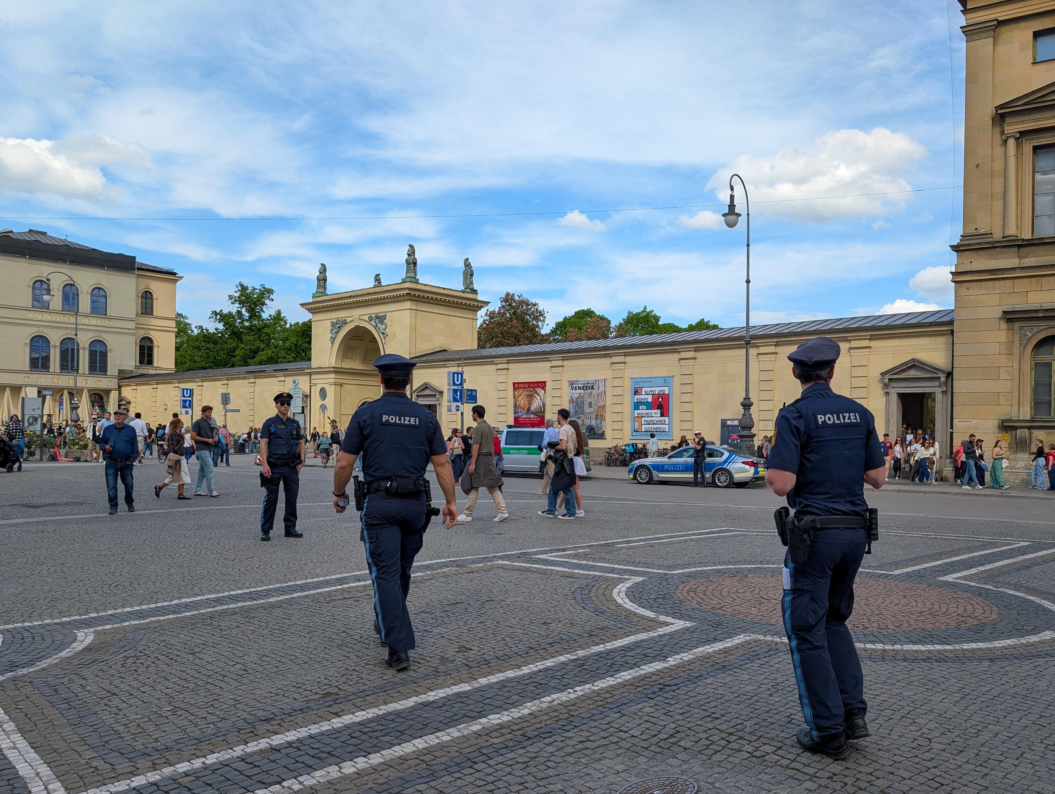 Zwei Polizeibeamte in blauer Uniform laufen auf dem Münchner Odeonsplatz auf einen dritten zu (Archiv-, Symbolbild).
