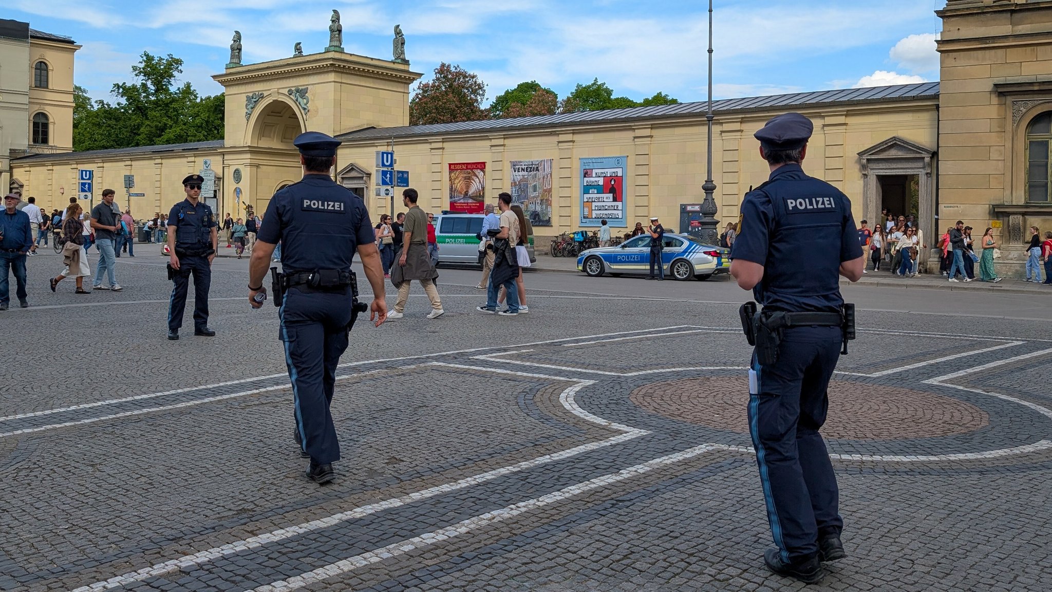 Zwei Polizeibeamte in blauer Uniform laufen auf dem Münchner Odeonsplatz auf einen dritten zu (Archiv-, Symbolbild).