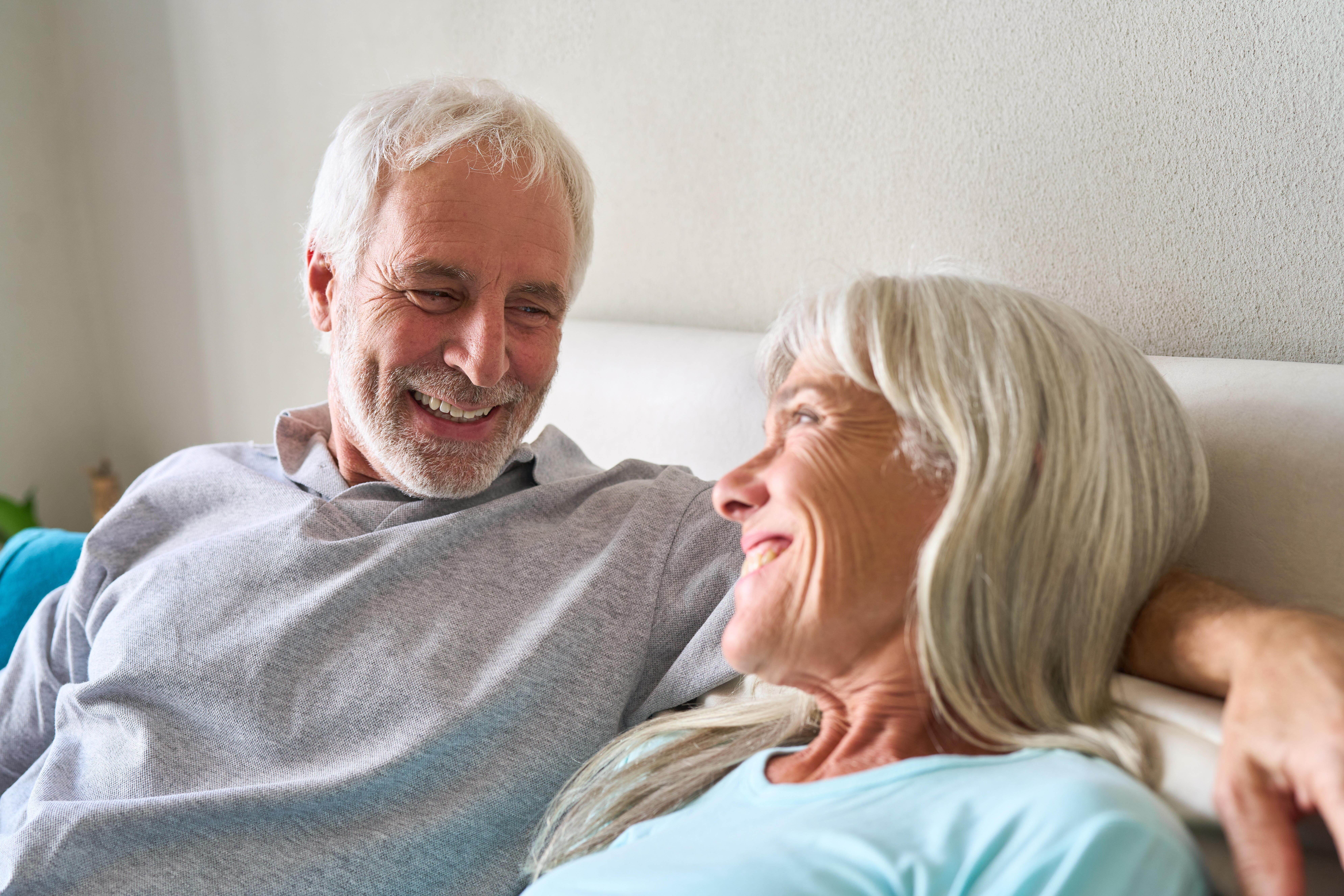 Senior Paar lächelt und lachen zusammen in einem komfortablen Innenbereich.