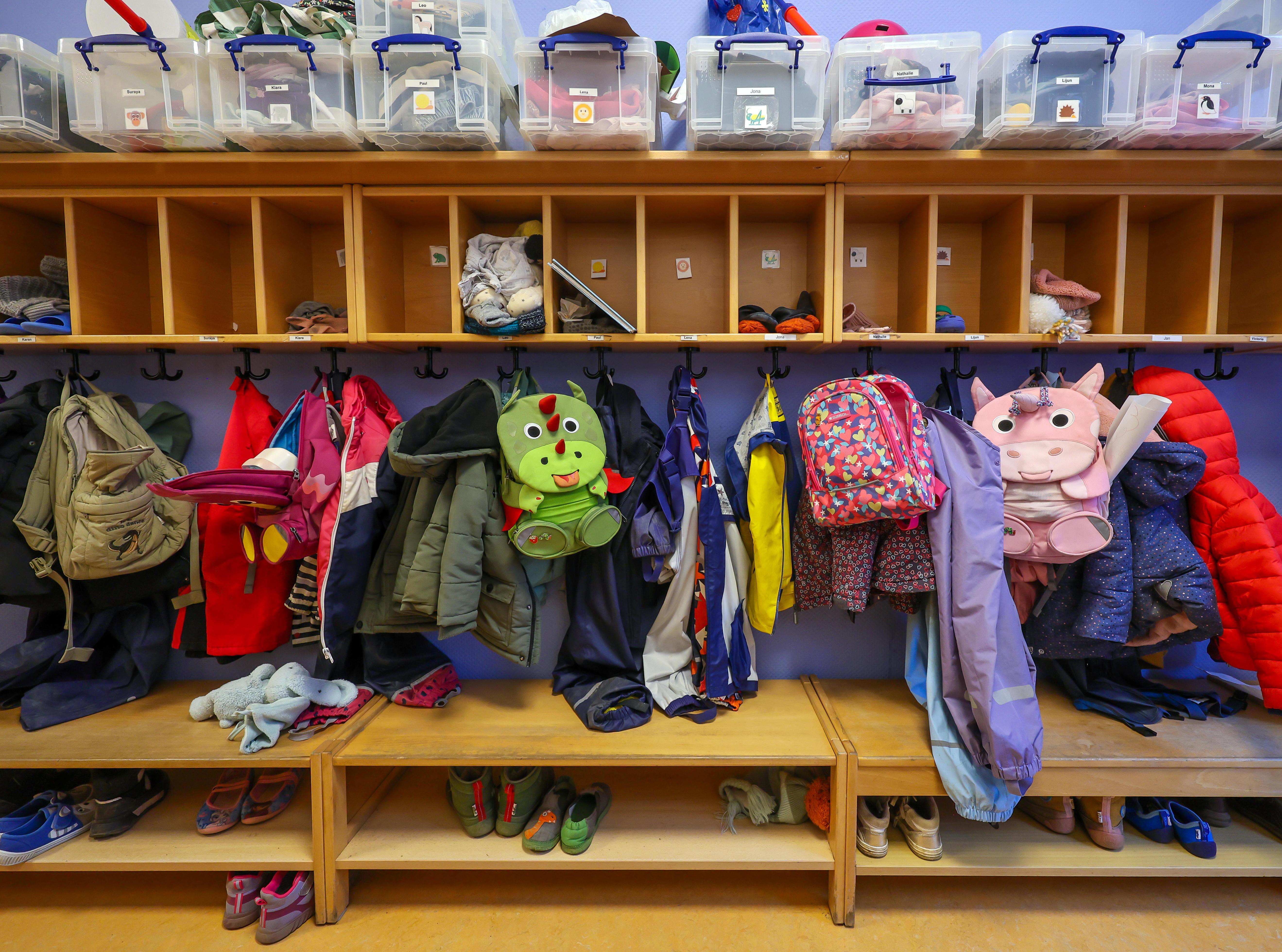  Symbolbild KITA. Mäntel, Jacken und Rucksäcke von Kindern hängen an einer Garderobe in einem Kindergarten.