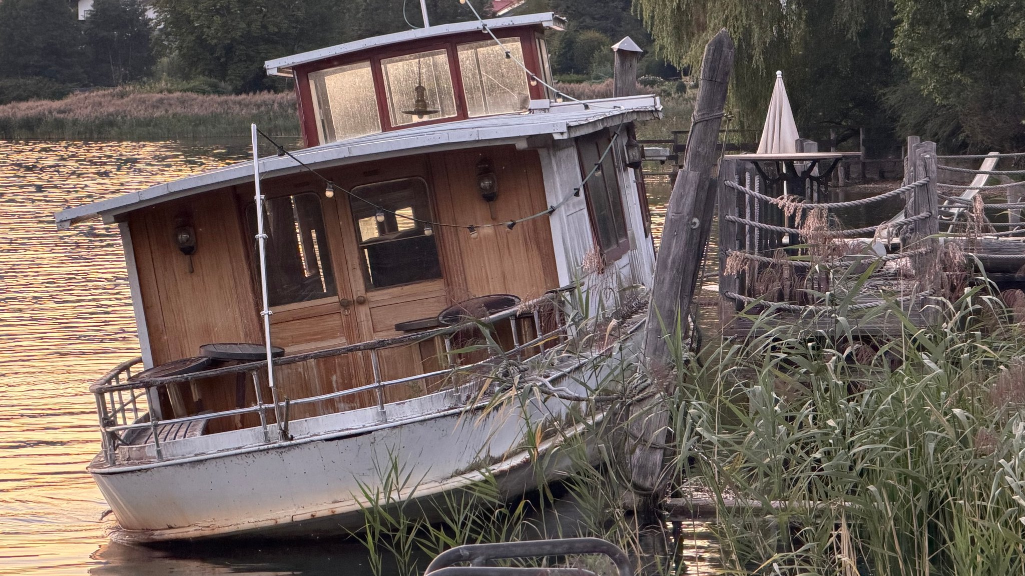 Halb im Wasser liegt ein Schiff mit deutlichen Schäden an Holz und Lack.