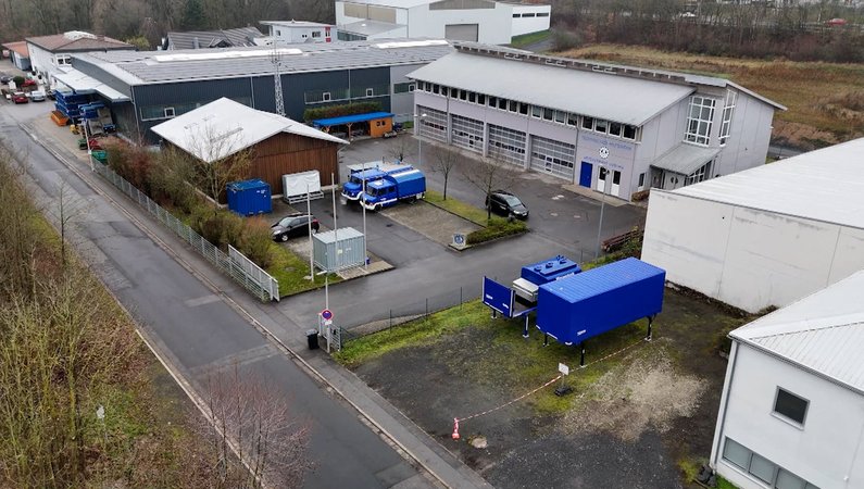 Vor Zweckbauten parken blaue Nutzfahrzeuge, betrachtet aus der Vogelperspektive. | Bild: BR24 Vor Zweckbauten parken blaue Nutzfahrzeuge, betrachtet aus der Vogelperspektive.
