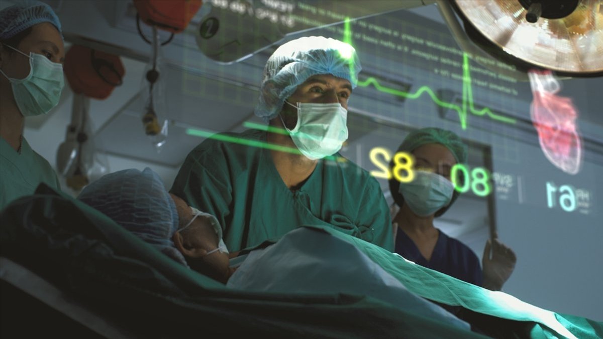 Ein Arzt in einem Operationssaal. Auf einem Bildschirm betrachtet er die angezeigten Vitalfunktionen eines Patienten. 