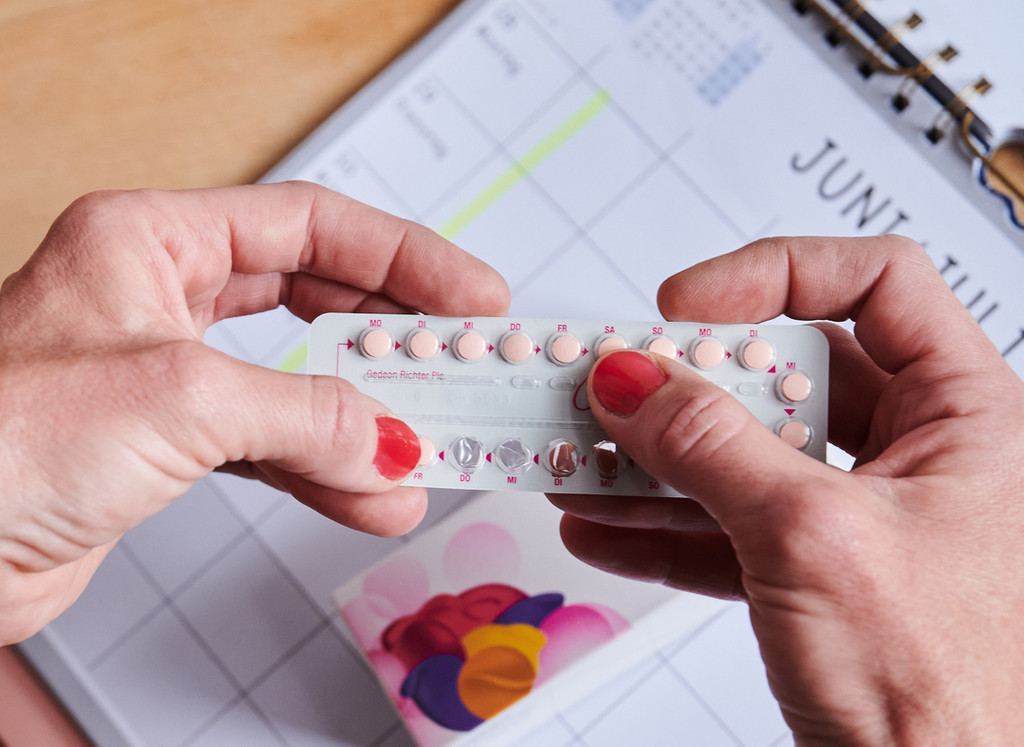 ber einem Kalender nimmt sich eine Frau die nächste Pille aus einer Monatspackung der Antibabypille.