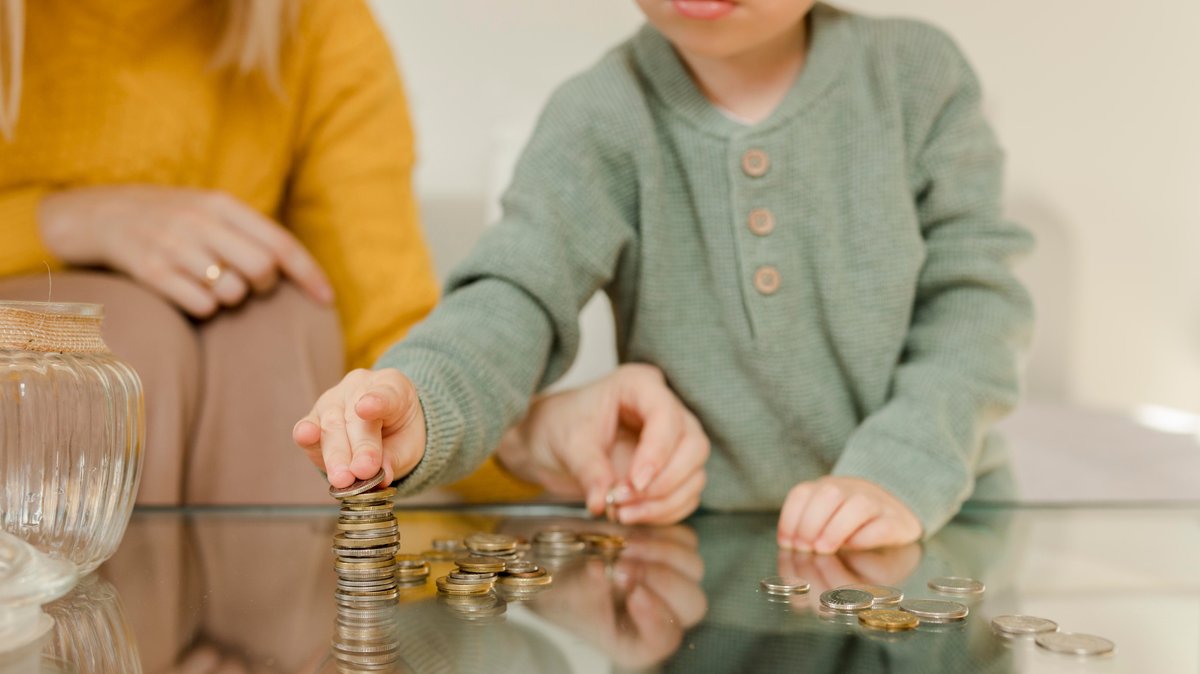 Eine Mutter und ihr Kind stapeln Münzen auf einem Tisch vor sich (Symbolbild)