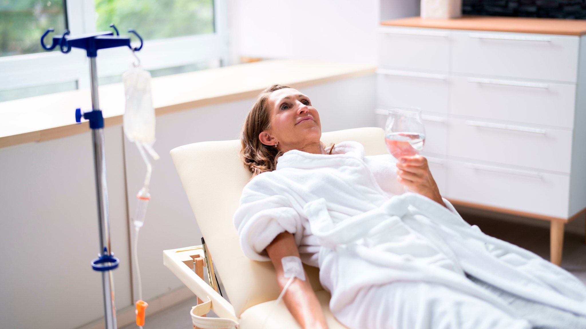 Eine Frau im weißen Bademantel erhält in einer Klinik eine Vitamin-Infusion in die Armbeuge. | Bild: picture alliance / Visually | Andriy Popov Eine Frau im weißen Bademantel erhält in einer Klinik eine Vitamin-Infusion in die Armbeuge.