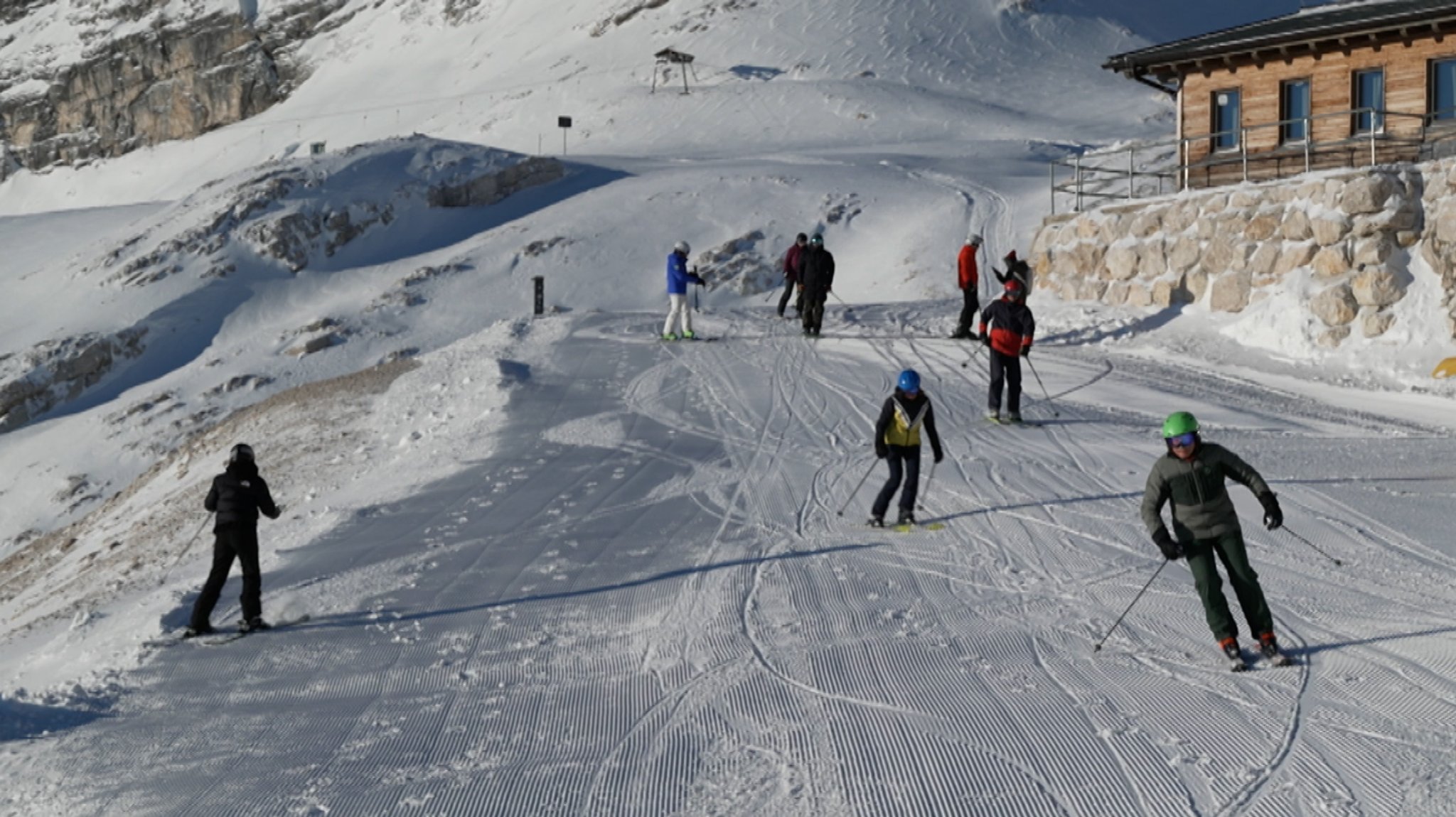 Zu sehen sind etwa zehn Skifahrer, die auf einer präparierten Piste nach unten kurven.